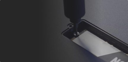 Prim-plan al feței inferioare din metal gri antracit a unui dispozitiv electronic, văzută de sus, ușor înclinată, prezentând o șurubelniță neagră introdusă în șurubul central al unei trape dreptunghiulare care lasă să se întrevadă un modul intern cu contacte aurii