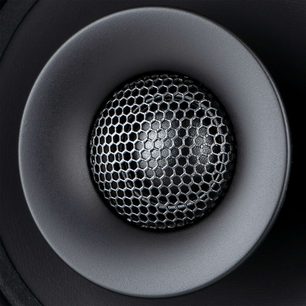 Haut-parleur rond noir vu de face dans un renfoncement circulaire gris foncé, grille de protection en nid d'abeille métallique devant