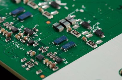 Green printed circuit board with numerous miniature electronic components soldered on, including resistors and capacitors