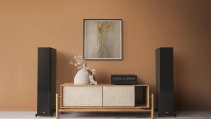 Lyst tremøbel med flettede dører, beige vase med grener, svart forsterker, 2 svarte høyttalere, innrammet abstrakt maleri