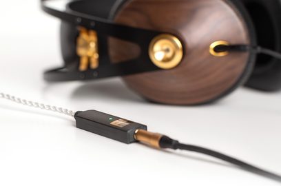 Bærbar iFi Audio GO Link audio-konverter i mørkt træ, tilsluttet et sort kabel, ved siden af et brunt hovedsæt