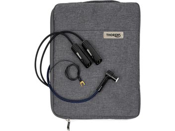 Pohled shora na kabel Thorens PhonoConnect PHS 150 DIN-XLR o délce 1,5 m v černé barvě s textilním opletením v modro-černém provedení, vybavený dvěma černými kovovými XLR konektory, ohnutým DIN konektorem a uzemňovacím vodičem s pozlacenou očkem, položený na šedém látkovém pouzdře.