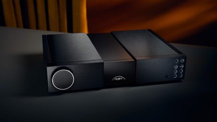 aparat audio din aluminiu negru periat, față frontală, buton rotativ circular iluminat, logo luminos centrat, șase butoane rotunde aliniate, intrare jack pentru căști
