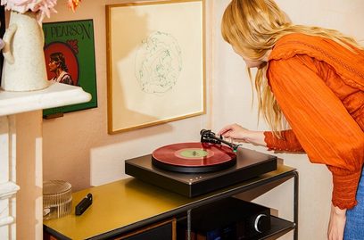 Cambridge Audio Alva ST hõbedane vinüülmängija, vaade ülalt. Punane vinüülplaat plaaditaldriku peal. Naine asetab kuuldenõela