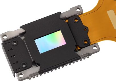 Componente electrónico rectangular con superficie reflectante multicolor, conector flexible naranja, vista desde arriba
