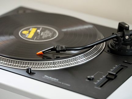 Juoda vinilinė plokštelių žaidyklė su galvute, adatėle ir uždėta viniline plokštele, artimas viršutinis šiek tiek įžambaus kampo vaizdas