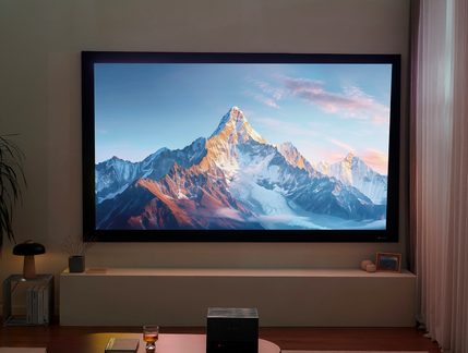 Televisor de pantalla gigante montado en la pared con marco negro que muestra un paisaje de montaña nevada en un salón moderno