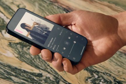 Hält ein schwarzes Smartphone mit einer Musikplayer-Oberfläche, Hintergrund aus marmoriertem Stein in Grün- und Beigetönen.