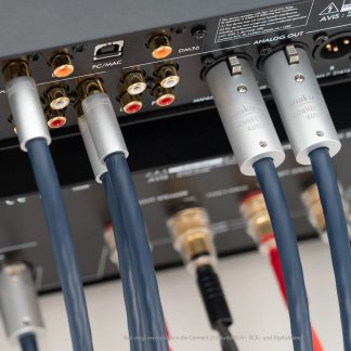Skrå bagfra-billede af bagenden af et lydapparat med tykke blå plastikbeklædte kabler, der er tilsluttet sølvfarvede metal-XLR-stik og forgyldte RCA-stik
