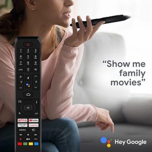 Ung kvinde set fra siden, der holder en sort fjernbetjening og taler til en smartphone og siger "Vis mig familiefilm"
