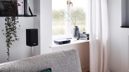 tilkoblet hi-fi-lydsystem med svart gulvstående høyttaler og nettverksspiller på vinduskarm i lyst stuerom
