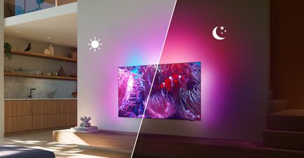 Black flat-screen TV with a slim metallic frame, front view, mounted on a light-colored wall, displaying a colorful coral image with a soft pink and blue backlit halo around the frame