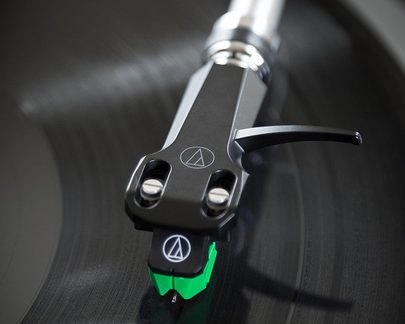 Doză phono Audio-Technica neagră și verde, prim-plan pe un disc de vinil în timpul redării