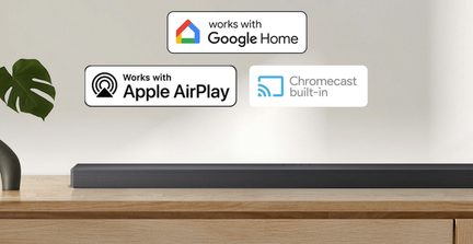 Barra sonora nera con corpo rettangolare in metallo con griglia, vista frontale, posizionata su un ripiano in legno chiaro con i loghi Google Home, Apple AirPlay e Chromecast visualizzati sopra