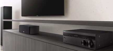 Vue latérale d'un téléviseur mural noir, enceinte noire, amplificateur Sony noir, meuble gris, mur gris clair