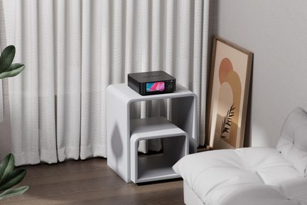Černý obdélníkový elektronický přístroj s matným kovovým pouzdrem, barevným předním displejem a otočným tlačítkem, prezentovaný v mírném tříčtvrtečním pohledu na bílé skládací stolku