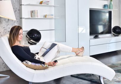 Kvinne som ligger på en hvit, buet sofa og ser på en TV-skjerm i en moderne stue med hvite møbler