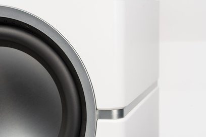 Subwoofer Dynamo 10 blanco lacado, vista cercana de una esquina superior derecha con borde redondeado y altavoz circular negro