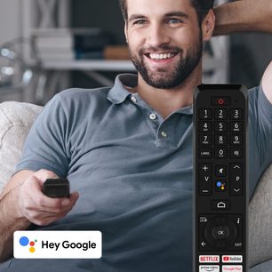Billedet viser en smilende mand, der holder en fjernbetjening og peger mod en skærm, der viser Google Assistants grænseflade