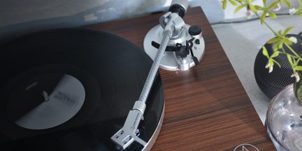 Giradischi con piatto nero, braccio di lettura argentato, base in legno, altoparlante sferico nero e vaso trasparente con fiori