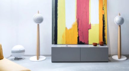 Par hvide gulvhøjttalere i lyst træ set forfra i en moderne stue med gråt tv-møbel og abstrakt maleri