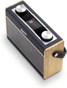 Rádio Roberts Rambler Max v tmavě modrém provedení, obdélníkový tvar s přední stranou v tmavě modré a bílé žebrované úpravě, světlé dřevěné boky, boční kožená černá rukojeť se šitím, dva velké stříbrné knoflíky a centrální displej na horní straně, pohled z tříčtvrtinového úhlu shora