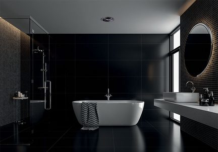 Vista frontale di un bagno contemporaneo, con pareti e pavimento in piastrelle nere lucide, vasca da bagno a isola bianca in materiale liscio al centro con asciugamano a motivo chevron grigio, lavabo sospeso in pietra chiara e specchio rotondo retroilluminato a destra, cabina doccia in vetro a sinistra.