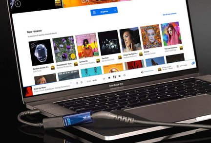 MacBook Pro in alluminio grigio, vista obliqua, schermo musicale, dongle audio USB blu metallizzato e cavo nero