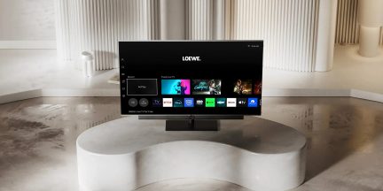 Černý chytrý televizor Loewe na středovém stojanu zobrazující streamovací rozhraní v moderním bílém interiéru