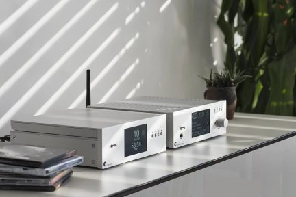 Hvid cd-afspiller og hi-fi-forstærker med sort skærm, drejeknap og antenne, set i trekvart vinkel på hvidt møbel