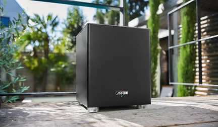 Subwoofer Canton cubico nero con piedini in metallo, posizionato all’esterno su un terrazzo in legno
