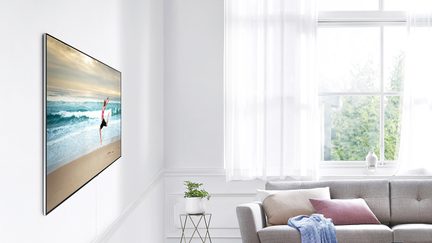 Veggmontert TV i en lys stue som viser en strandscene med et rødt flagg, sett forfra