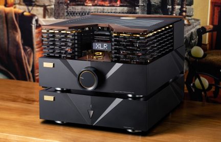 Hi-Fi audio zesilovač s elektronkami složený ze dvou černých matných kovových bloků s pozlacenými deskami a lemováním, velkým kruhovým tlačítkem obklopeným zlatem a malým displejem „XLR“ na předním panelu, horní část s perforovaným krytem odhalujícím elektrony a větraným dřevěným krytem, pohled z pravého předního tříčtvrtečního úhlu