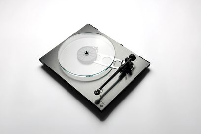 Toca-discos hi-fi Rega Planar 3 RS com prato de vidro transparente, braço de leitura preto e base retangular cinza visto de cima.