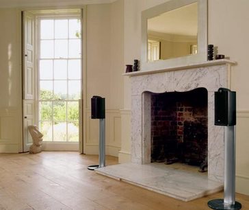 To sorte, høje Bowers & Wilkins XT2 gulvhøjttalere står på hver side af en marmorkamin i et indendørs miljø