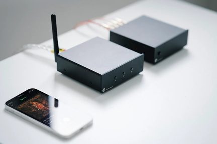 Czarny bezprzewodowy odbiornik audio z anteną i kompaktową obudową, stojący na stole obok smartfona
