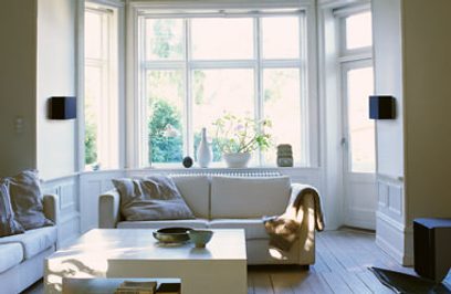 Lyst stue med hvid sofa, sofabord, store vinduer, grønne planter, sorte lamper og lyst trægulv
