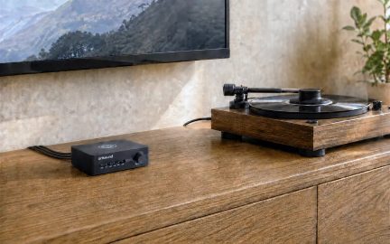 Компактен черен усилвател ArtSound с копче за силата на звука, до грамофон върху кафява мебел