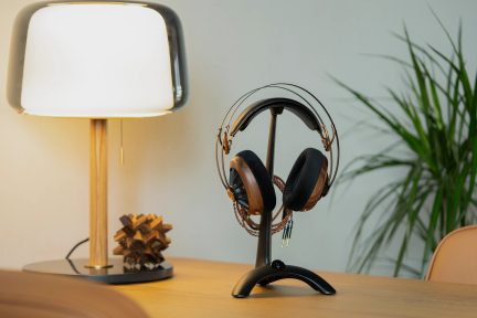 Hvit lampe på trebord, hodetelefoner på svart stativ, grønn plante i bakgrunnen, trepuslespill på bordet