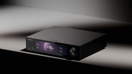 Matně černé hliníkové audio zařízení, pohled zepředu v tříčtvrtečním úhlu, středový displej −15 dB, otočný ovladač vpravo, sluchátkový výstup vlevo
