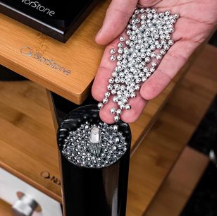 Silberne Metallkugeln, die in einem Kreis auf einer Hand angeordnet sind, die ein schwarzes Holzgehäuse mit dem eingravierten Logo "Norstone" hält
