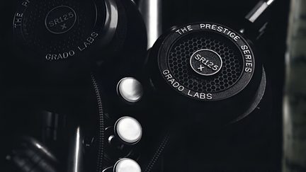 Øreklokke på sort hovedtelefon, åben konstruktion med bikubemønstret metalgitter, med påtryk 'GRADO LABS' og 'SR125 X', set i skrå vinkel