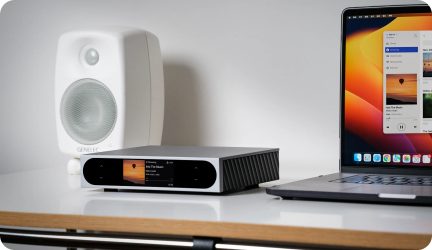 Lettore audio in alluminio spazzolato grigio con frontale nero lucido, dotato di schermo a colori e comandi touch, alette di dissipazione nere visibili sul lato destro, vista tre quarti anteriore