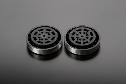 Dois discos metálicos circulares com padrões radiais pretos em um fundo cinza, vistos de frente sobre uma superfície cinza lisa