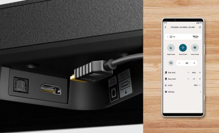 Vista cercana de un conector HDMI insertado en un puerto, smartphone mostrando interfaz de audio sobre superficie de madera clara