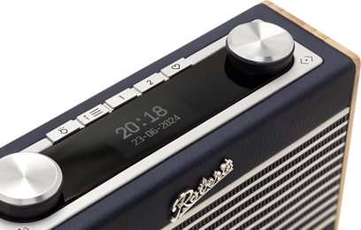 Radio da tavolo Roberts Rambler Uno blu navy, custodia rivestita in pelle granulata con bordi in legno chiaro, griglia frontale metallica argentata, due grandi pulsanti rotativi in alluminio e fila di tasti sul display digitale, vista superiore a tre quarti