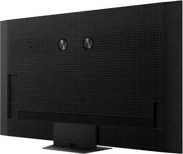 Sned bakre vy av TCL 85C8K högupplöst TV, svart chassi med rutmönstrad plast, två centrerade cirkulära metallskivor och rektangulär metallfot