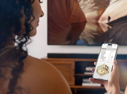 hátulról látható nő, aki okostelefonos alkalmazással irányítja a soundbart és a TV-t egy modern nappaliban