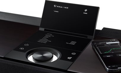 Primare Allt-i-ett, svart hi-fi-system, glasfront med uppfällbar skärm, stor ratt och touchknappar, sned vy