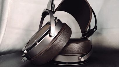 Cuffia aperta STAX SR-X9000 in pelle marrone e metallo argentato, vista da tre quarti posteriore su sfondo grigio chiaro
